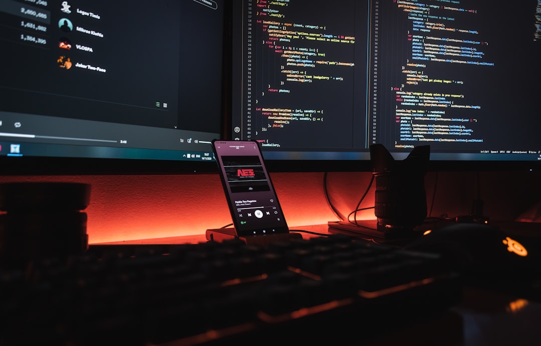 【Kiro】V3アップデート！セッション管理とクラウド同期機能を徹底解説 - A smartphone displaying music on a desk with computer monitors showing code